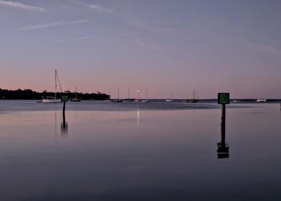 Quiet "blue hour" view opposite the approaching sunrise where a wide water meets an even larger waterway beneath blue and purple skies.