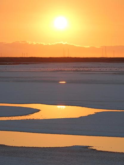 Sunset with salt flats and a small bodies of water reflecting the orange sky