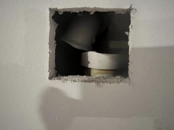 A small rectangular hole in a wall reveals the pipe elbow on top tuned and disconnected from the sump pipe discharge pipe below.