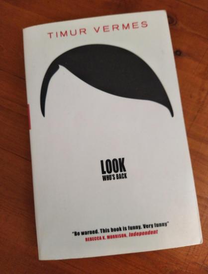 Cover of "Look Who's Back" by Timur Vermes with a silhouette of Adolf Hitler's hairstyle and the book title in place of a toothbrush moustache.