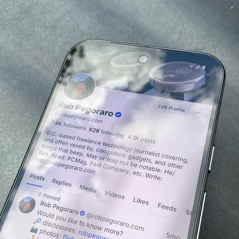 My phone with the Bluesky app open, showing my profile and its new checkmark. The phone's screen reflects a partly cloudy sky, with a streak of blue overlapping the checkmark icon.