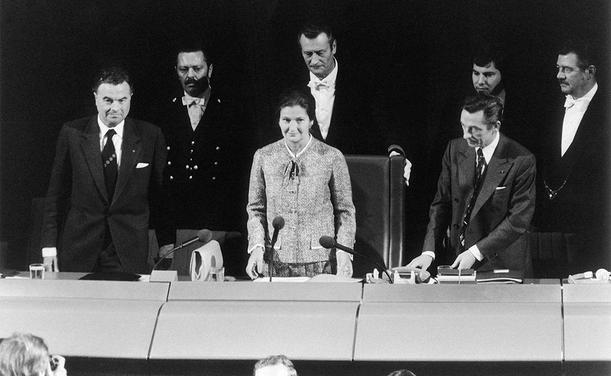 Simone Veil taking up the Presidency. She is a white woman. Six white men are standing beside or behind her.
