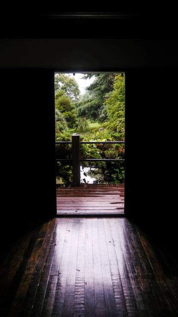 Photograph of the inside of a dark Japanese style house looking out into a garden area. Light is flooding in onto the floor.