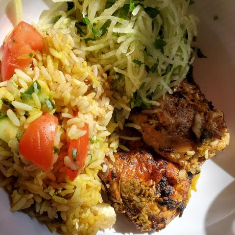 Bowl of jerk chicken, rice & beans with cucumber & tomatoes & some papaya salad.