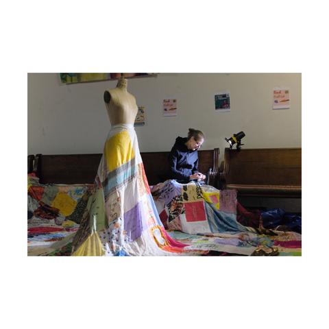 Picture of a woman weaving and stitching pieces of cloth in different colors and textures, which were written by women with their personal stories.