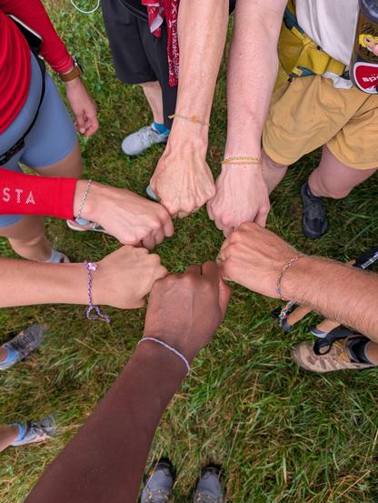 Six hands in a circle, each with a different color bracelet. Sold to us by two girls who set up shop on the Camino