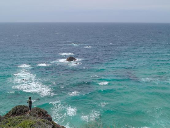 Woman standing at the end of a cliff with the blue ocean filling most of the fram