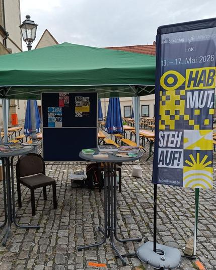 Ein Messestand mit einem Schirm, einer Pinnwand und einem Banner mit der Aufschrift "Hab Mut, steh auf".