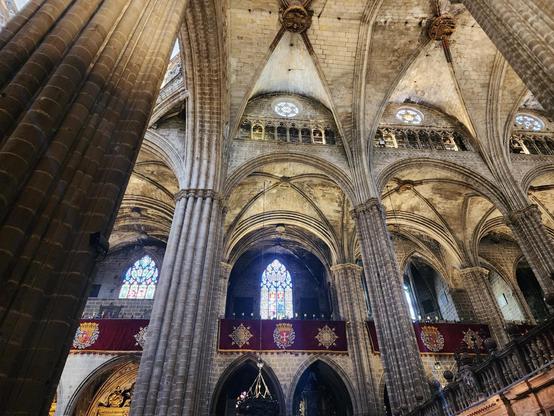 looking up at the stained glass windows from the center of the cathedral, their small size suggesting the building's huge proportions. at top is a row of three roundels and below is a row of larger pointed arch windows. interspersed among the windows are several ribbed columns holding up vaulted ceilings.