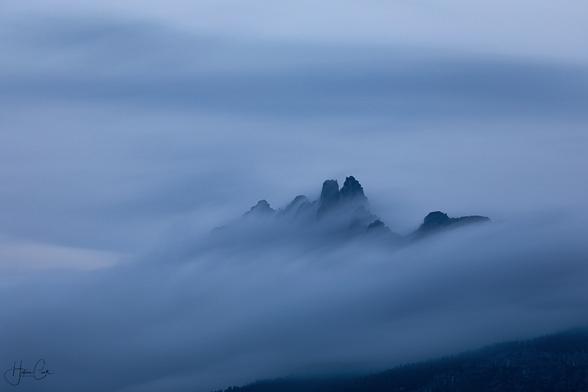 Tiny black mountain peaks in the distance poke out of a smooth sea of clouds at blue hour in the evening in the Dolomite mountains.