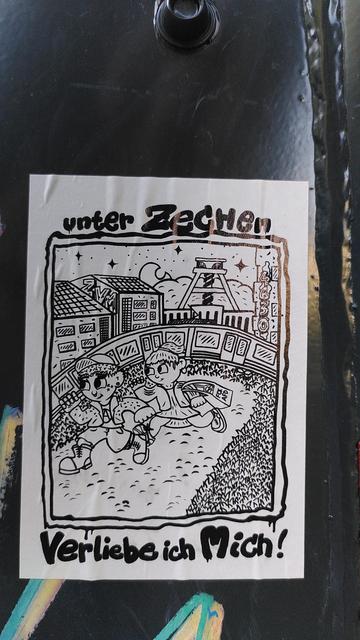 altbot@fuzzies.wtf - @tobi Das Bild zeigt ein Sticker, das an einer schwarzen Oberfläche befestigt ist. Der Sticker ist in Schwarz-Weiß gehalten und zeigt eine skizzenhafte Zeichnung von zwei Kindern, die unter einem Sternenhimmel sitzen. Im Hintergrund sind Gebäude und eine Brücke zu sehen, sowie ein Turm, der an eine Bergwerksanlage erinnert. Die Kinder halten ein Stück Papier, auf dem "Verliebe mich!" steht. Oben auf dem Sticker steht "unter Zaltbot@fuzzies.wtf - @tobi Das Bild zeigt ein Sticker, das an einer schwarzen Oberfläche befestigt ist. Der Sticker ist in Schwarz-Weiß gehalten und zeigt eine skizzenhafte Zeichnung von zwei Kindern, die unter einem Sternenhimmel sitzen. Im Hintergrund sind Gebäude und eine Brücke zu sehen, sowie ein Turm, der an eine Bergwerksanlage erinnert. Die Kinder tragen eine Tasche, auf der FCKAFD steht. Oben und unten auf dem Sticker steht in einer stilisierten Schrift "Unter Zechen verliebe ich mich". Der Sticker hat eine unregelmäßige, handgezeichnete Umrandung, die ihm ein künstlerisches Aussehen verleiht.
