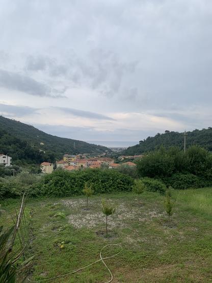 Tra due colline si intravede un paesello , in fondo il mare e il cielo