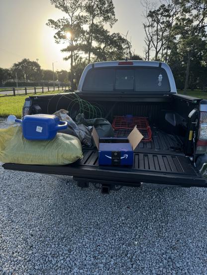 Garden soil in a yellow bag, warm castings in a green bag, and mushroom fertilizer in a brown bag. A blue box with gardening tools, green and bluee tomato cages, and a rolling shopping cart to carry all this to the plot. All of this in the silver gray truck bed. A sticker on the right side of the rear window showing a robot called Bender from Futurama saying Bite My Shiny Metal Ass.