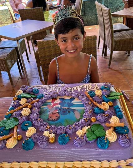 A young boy with a beautiful Lilo & Stitch birthday cake looking so happy wearing a dress and tiara