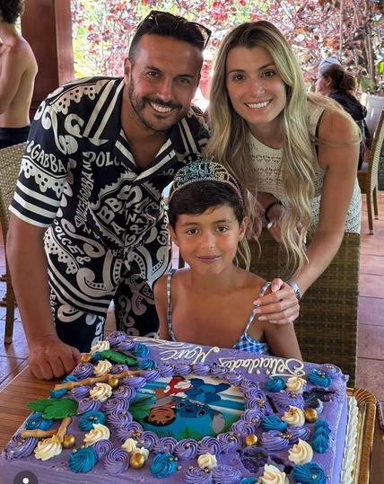 A young boy wearing a dress and tiara with his parents behind him looking so happy and supportive