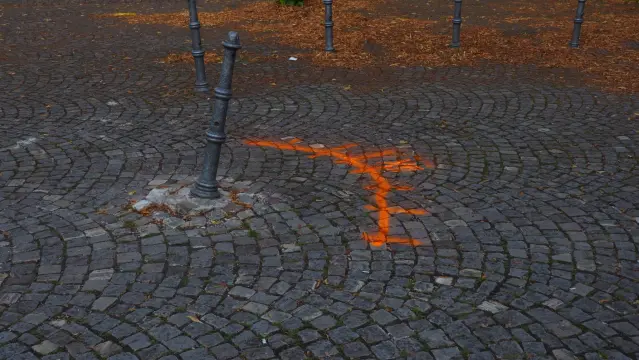 Schief stehender Poller im Kopfsteinpflaster. Mit orangener Farbe ist ein Bogen und die römische Zahl 12  auf das Pflaster gesprüht worden.