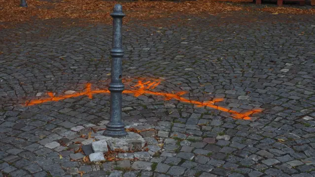 Schief stehender Poller im Kopfsteinpflaster. Mit orangener Farbe ist ein Bogen und die römische Zahl 12  auf das Pflaster gesprüht worden.