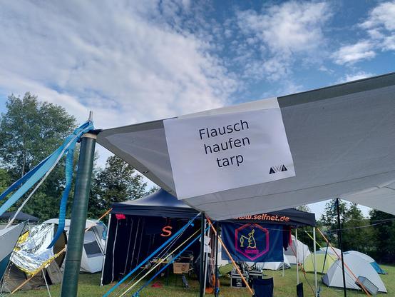 Ein großes weißes Tarp an dem ein Schild aufgehängt wurde mit der Aufschrift "Flauschehaufentarp".