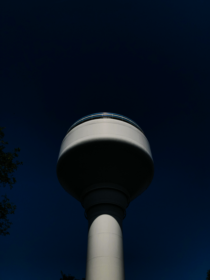 A low exposure colour view looking upwards at a tall white space age looking water tower in Amsterdam against a cleardark blue sky.