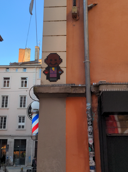 En hauteur au-dessus d'une corniche à un coin de rue, une mosaïque représente Morpheus de Matrix en train de proposer la pilule rouge et la pilule bleue, dans le style de InTheWoup mais non signé.