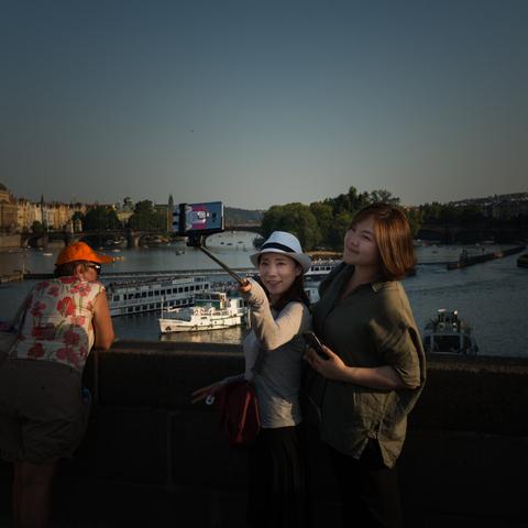 Portrait of a couple of tourists making a selfie of the both of them together. One hold a stick, the other is next to her. They're on a bridge in Prague