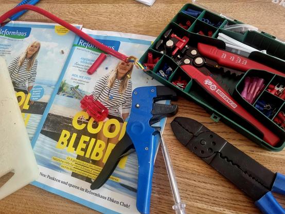 Kaputtes Kabel und diverses Elektrobastelzeug, als Unterlage ein Werbeblatt vom Reformhaus mit dem Titel "COOL BLEIBEN"