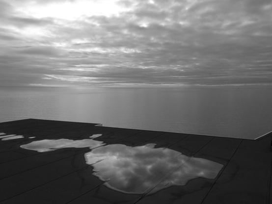 A view of the Irish Sea with puddles on the ground in the foreground. (Version françæ) Vue sur l’étendue dal Mer d’Irlande, avec des flaques sur læ sol al premiær plan.