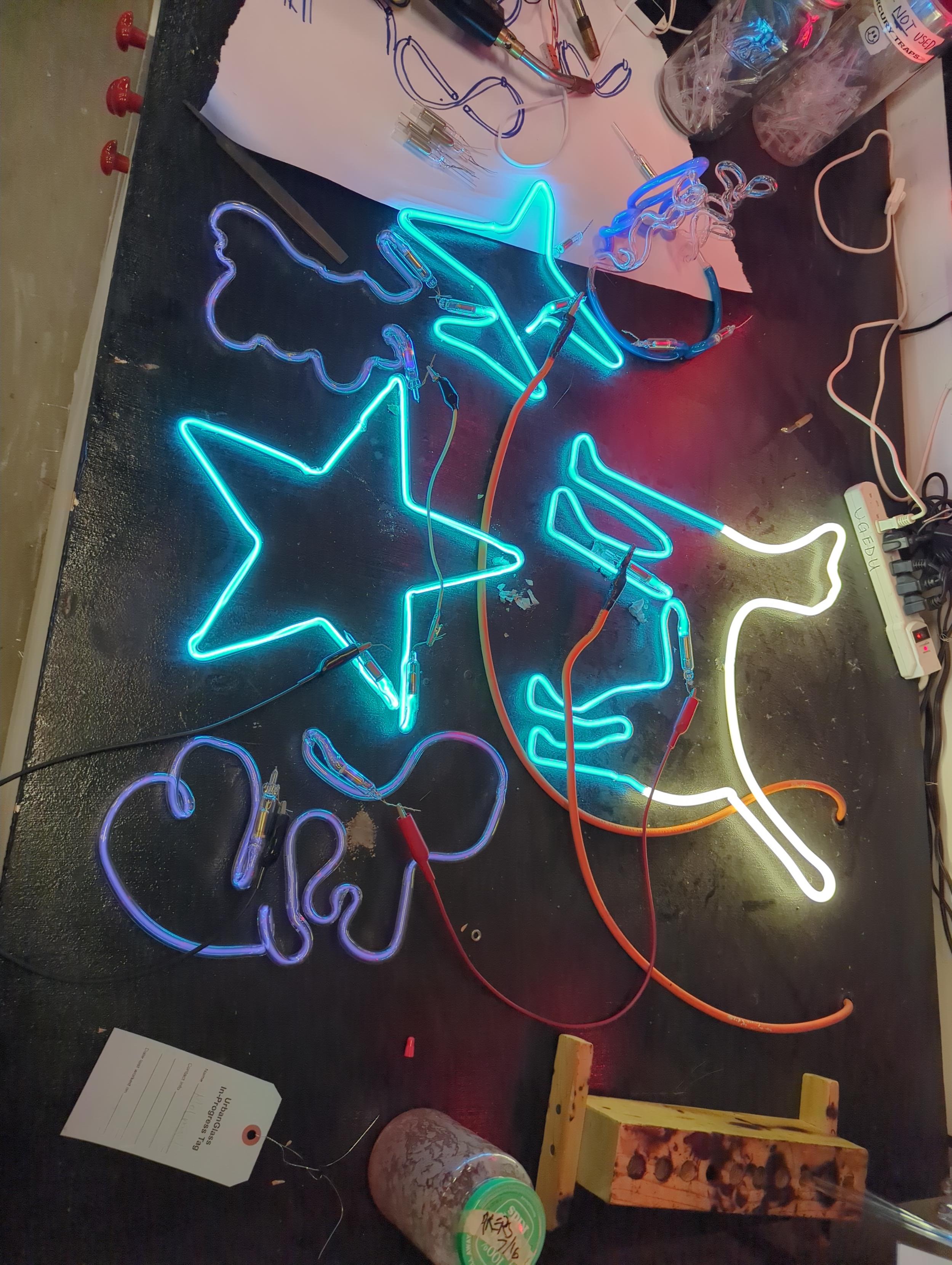 A variety of Argon and Argon Mercury student tubes on the black aging table at Urbanglass. Recognizable shapes include and white and blue dog, a blue star and blue plane