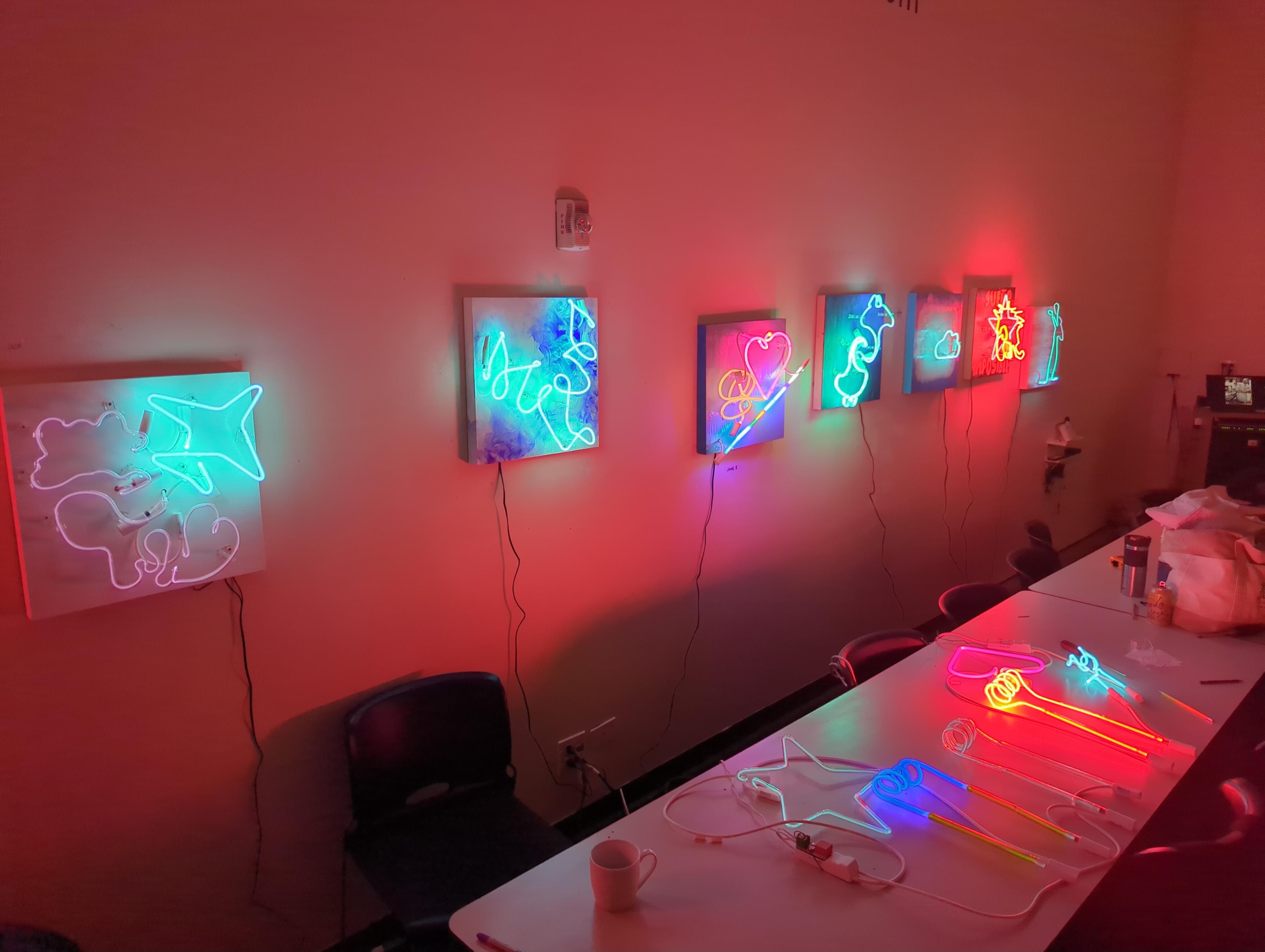 A selection of student designs on boards on the wall an off of boards on the table. The room glows a red pink color