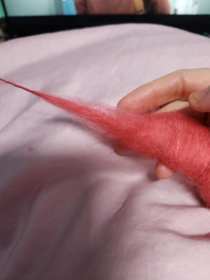A coil of wool and silk being spun. The fiber is a vivid shade of orange-pink.