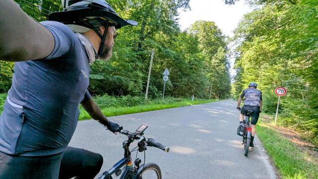 Ein Radfahrer fotografiert sich auf dem Rad von schräg hinten. Zu sehen ist sein gerader Lenker, sein Körper. Vor ihm fährt ein weiterer Radfahrer auf einer Straße, auf der maximal 70 km/h gefahren werden dürfen.