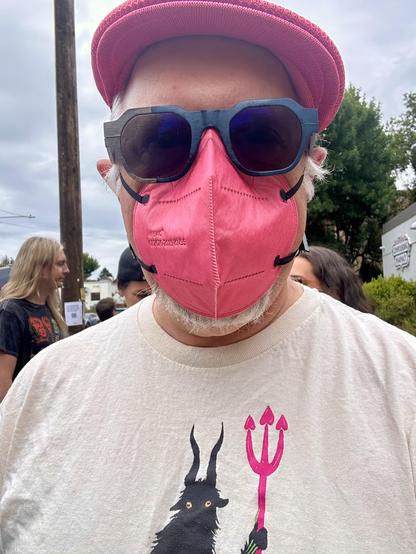 A selfie featuring a bright pink flat cap, bright pink kn95 mask, and a t shirt with a demon holding a bright pink trident.