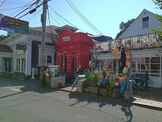 A photo of a Commercial Street streetscape. A banner hangs across the road reading "make America gay again." A small shop with a red painted front has a marquee reading "LOVE N HAPPINESS". The shop next door is festooned with lobster trap buoys.
