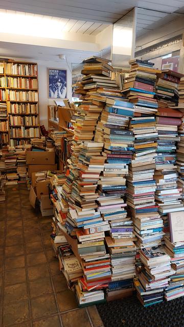 Tweedehands boeken in hoge stapels, de meeste op de vloer.