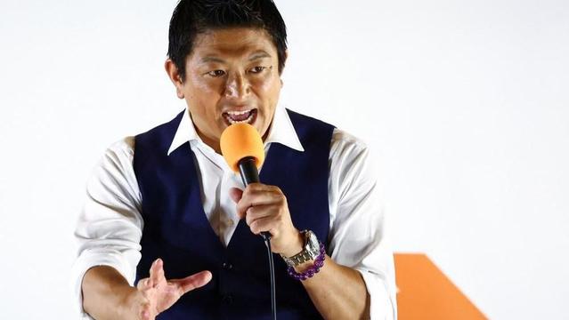 Japan's Sanseito party leader Sohei Kamiya, standing in front of his party's banner holding an orange mic, speaks to supporters on 20 July, the last day of campaigning