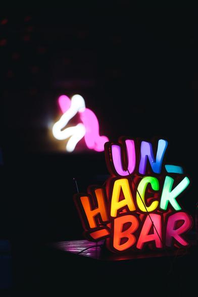 Das  bunt beleuchtete 3D-gedruckte Unhackbar Logo steht auf einer Theke. Im Hintergrund die Umrisse eines leuchtenden Einhorn-Kopf. Der Rest des Bildes ist in Dunkelheit gehüllt.
