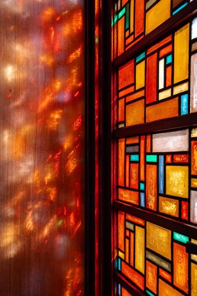 Art deco stained-glass window with geometric motifs designed by Jaap Gidding, at the Buuren museum in Brussels. The warm colours, punctuated by a touch of green, filter the light gently, producing dreamy reflections on the wooden window frame inside the house.