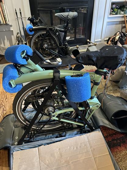 A folded Brompton bicycle ready to be tucked into a travel bag for a flight.