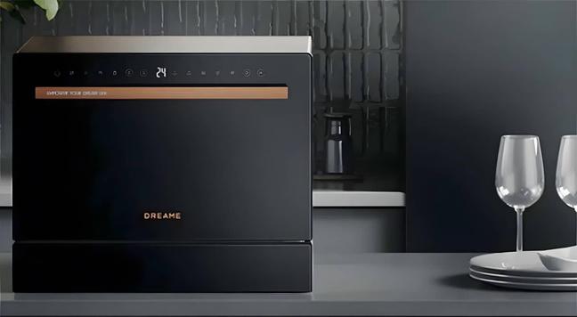 Schwarze Dreame Z2000 Spülmaschine steht auf einer grauen Küchenablage, rechts daneben Weingläser und weiße Teller. Foto (c) Dreame.