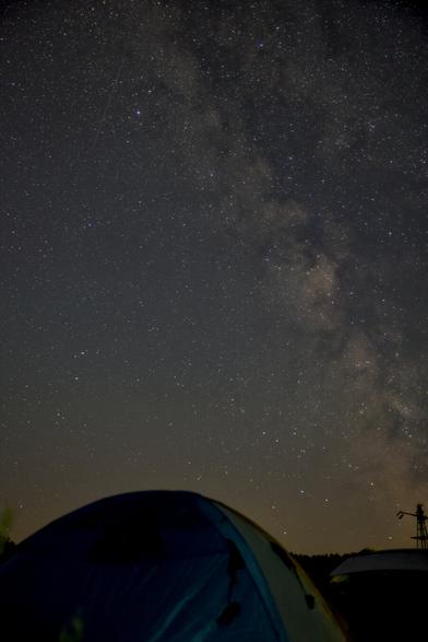 bild im hochvormat,
im vordergrund ein aufgebautes dunkles zelt, dahinter der nachthimmel, worüber sich die miclhstraße zieht