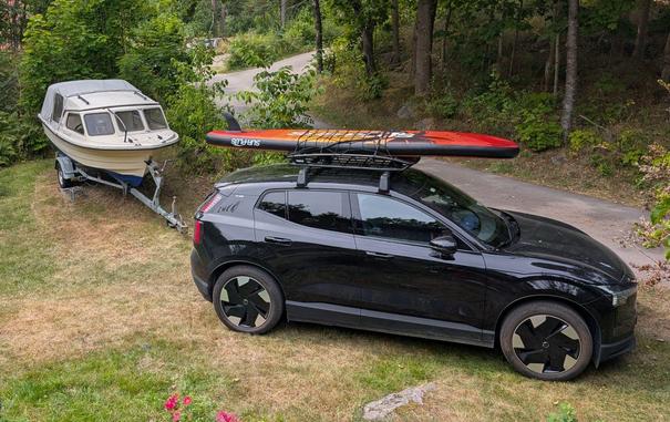 Bil med SUP på taket og en båt på henger i bakgrunn.