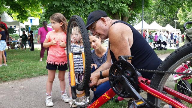 Un homme aide une mère de famille accompagnée de ses deux filles à régler les freins de son vélo.