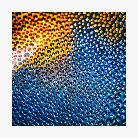 The photo is a close-up view of a surface (a water bottle) covered in numerous small, round droplets.  These droplets have a gradient of colour - they transition from warm oranges and yellows at the top to cool blues at the bottom.