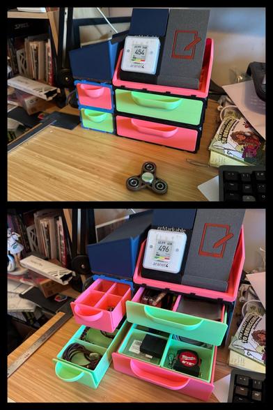 Two photos of 3D printed drawers.

There are 4 drawers with faces that are either bright pink or neon green. They look like something you’d find in a little girl’s room. 

There are two levels of drawers. All the drawers are one grid high. On the left is a two grid wide drawer. On the right is a four grid wide drawer. All the drawers are five grids deep.

In the top photo all the doors are closed. In the bottom photo, they are all pulled out a little and you can see a wide variety of divided inserts. 

There is a fidget spinner on the desk in front of it. On top of the four by five drawers are two of my 3D printed stands for the reMarkable tablet