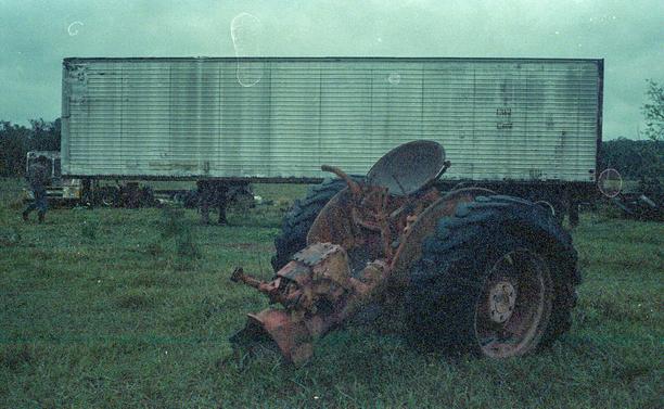the rear half of a tractor set in a field in front of a semi trailer.