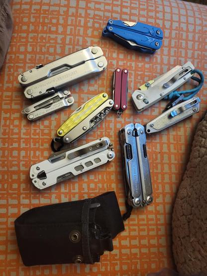 A collection of 9 different Leatherman tools jumbled together on an orange couch cushion.