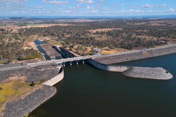 An aerial photo of the Wivenhoe Dam spillway, looking from above the lake, over the damn wall on along the river flowing out the other side