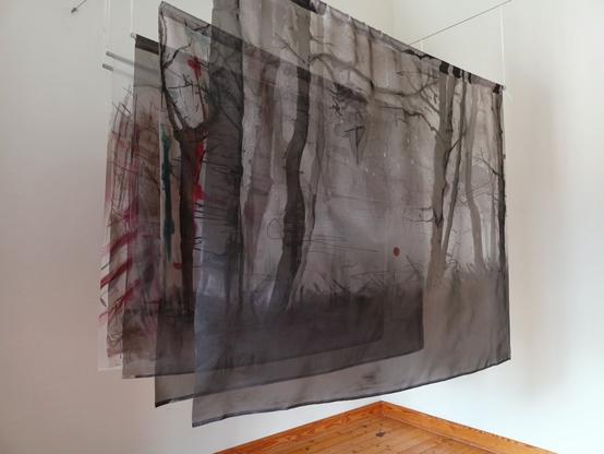 We see a work by the German artist Eleonora Damme, who has painted various lengths of fabric with ink. The panels are mounted one behind the other.