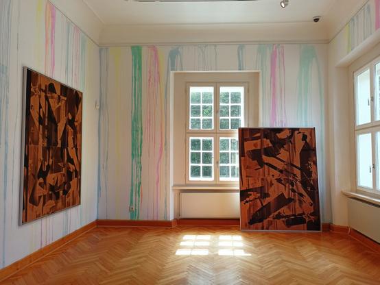 View into an exhibition room in which two contemporary abstract paintings are presented, one hanging on the wall, the other on the floor. Colour runs from the walls in different shades.