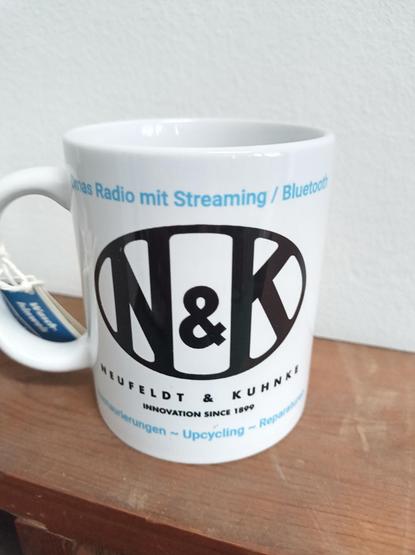 Neuer Kaffeebecher von Neufeldt & Kuhnke!
Oben: Omas Radio mit Streaming Bluetooth
Mitte: N&K Logo
Darunter : NEUFELDT & KUHNKE
Innovation since 1899
Unten : Restaurierungen ~ Upcycling ~ Reparaturen